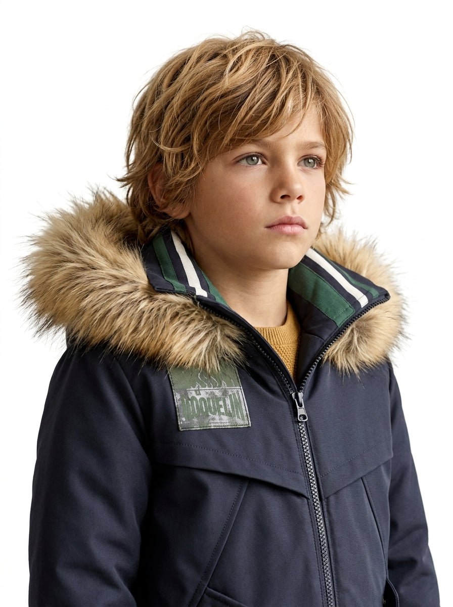 Detalle editorial del abrigo Outside azul marino de niño con cuello listado verde blanco y azul y capucha de pelo sintético