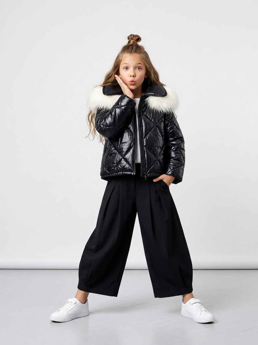 Niña con abrigo Blackout negro brillante, pantalón negro ancho y zapatillas blancas en editorial de estudio