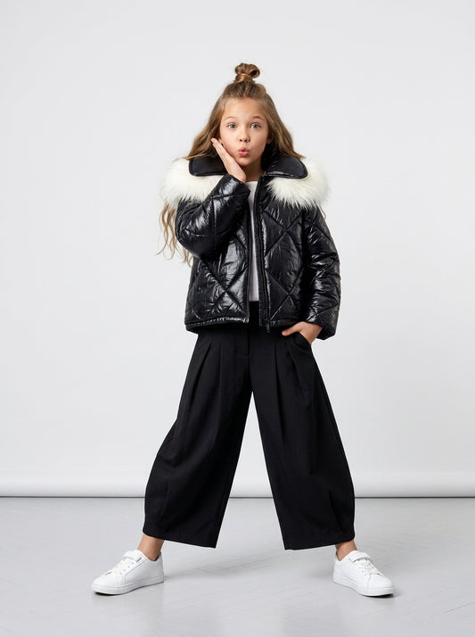 Niña con abrigo Blackout negro brillante, pantalón negro ancho y zapatillas blancas en editorial de estudio